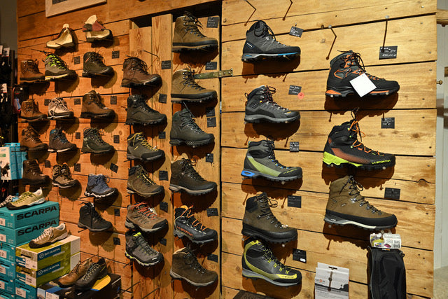 Holzwand voller Wanderstiefel, jedes Paar mit handgeschriebenem Schild